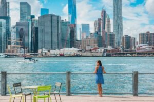 New York city Manhattan skyline seen from Brooklyn waterfront - woman enjoying view. American people walking enjoying view of Manhattan over the Hudson river from the Brooklyn side. NYC cityscape