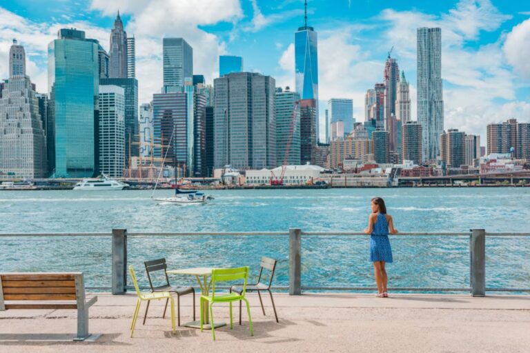 New York city Manhattan skyline seen from Brooklyn waterfront - woman enjoying view. American people walking enjoying view of Manhattan over the Hudson river from the Brooklyn side. NYC cityscape